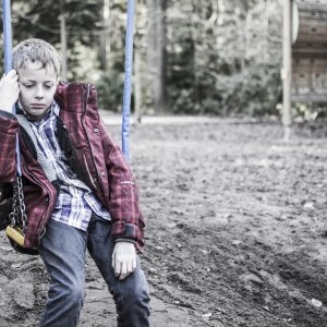 Sad or depressed boy sitting in playground swing